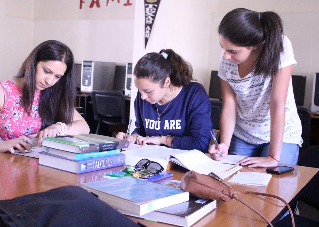 Three young women studying together at a table with books and personal items.