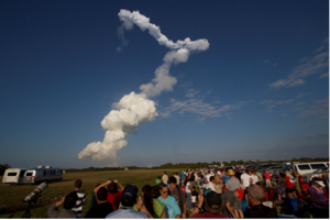 A trail of smoke in the sky above people.